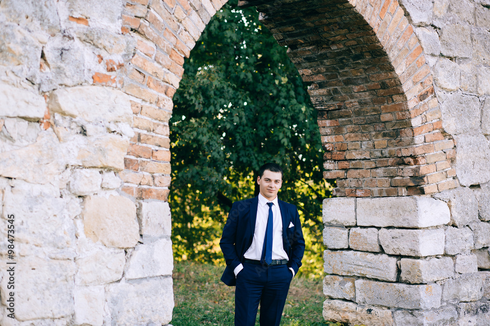 confident, cute groom man in a stylish business suit, outdoors, autumn. Portrait of the groom in the park on their wedding day. Rich groom man on their wedding day