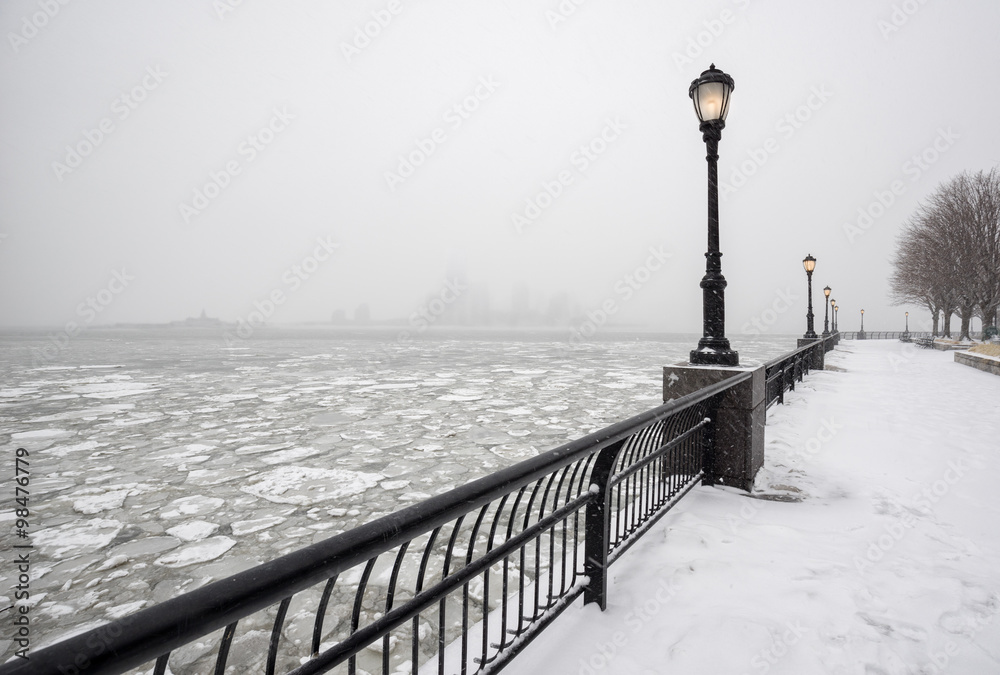 Naklejka premium Frozen Hudson River from snowy Battery Park towards Jersey City in fog. A silent winter day in New York City.