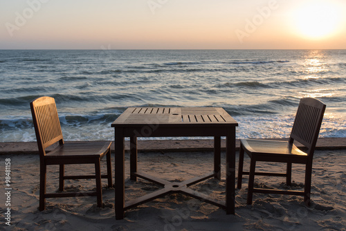 Wooden chairs on the beach at sunrise with a tropical sea background