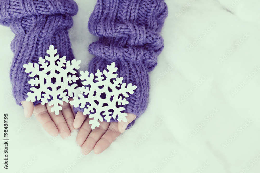 Woman hands in light teal knitted mittens are holding snowflakes