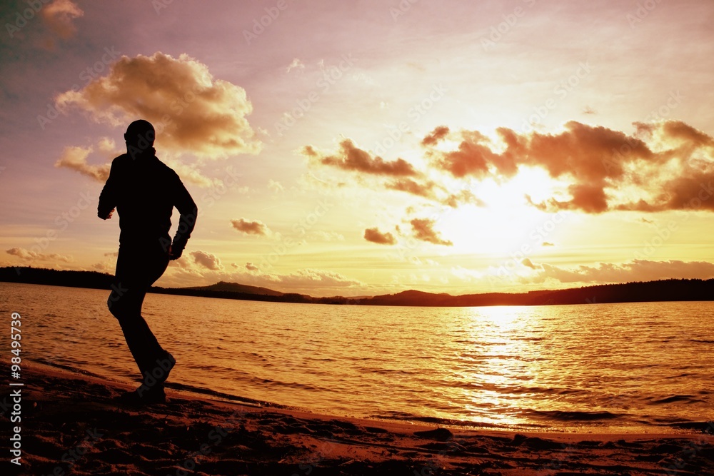Tall sportsman run along sea coast of sunrise behind, empty beach