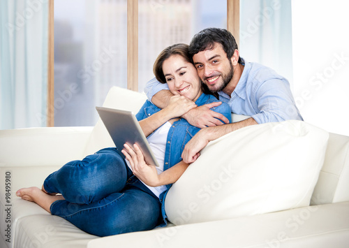 beautiful latin couple in love lying together on living room sofa couch enjoying using digital tablet