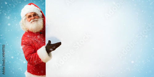 Santa Claus holding copyspace blank sign for Your Text / Merry Christmas & New Year's Eve concept / Closeup on blurred blue background. © Romario Ien