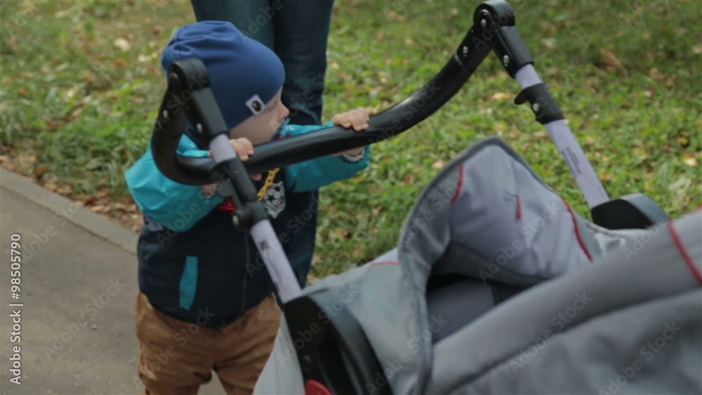 Small child toddler boy pushing a carriage in the park, slowmotion Small child toddler boy pushing a carriage in the park, slowmotion