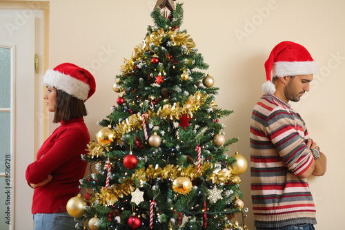 Unhappy young couple standing back to back next to the Christmas tree