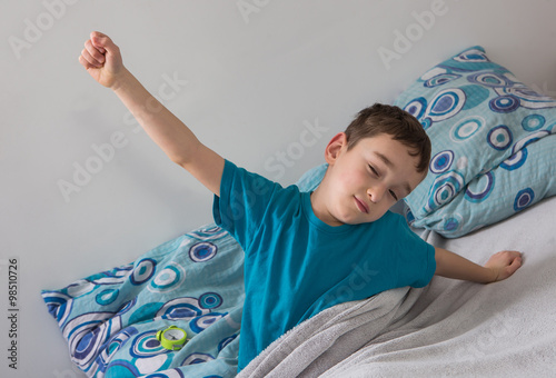 The small boy  with alarm clock in  the bed 
 photo