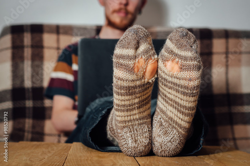 Young man working with laptop in holey socks