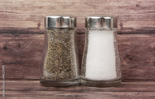 Salt and peppercorn powder in glass condiment shaker over wooden background