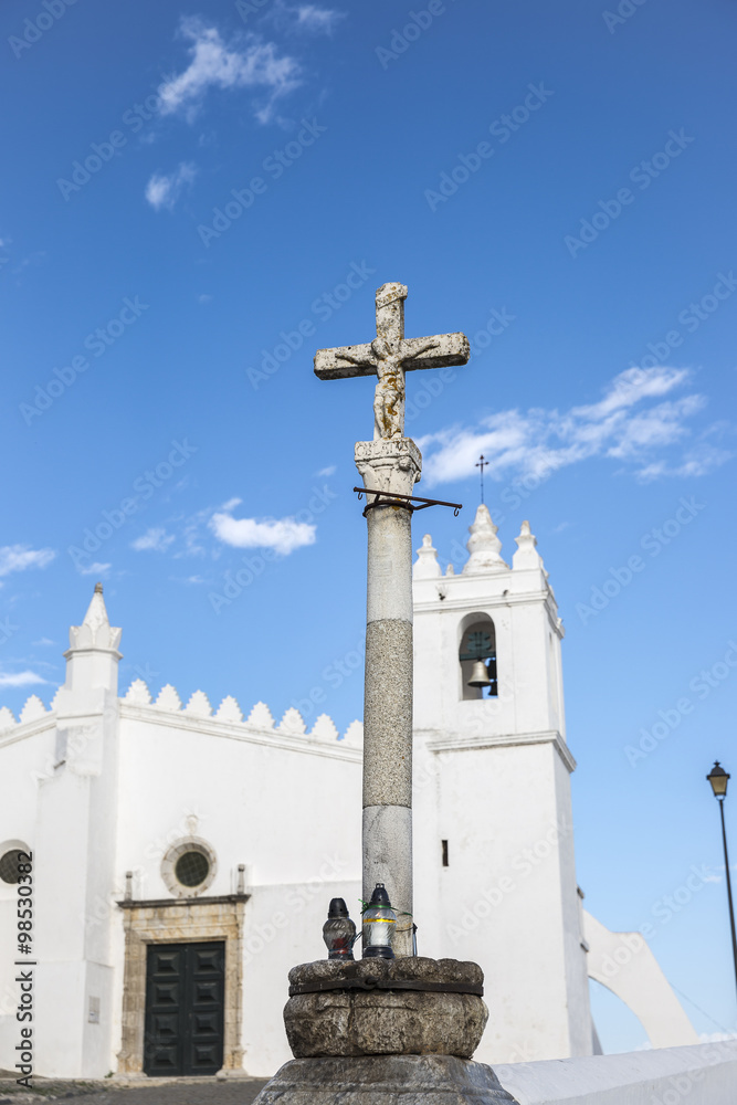 stone pillory with Christ on the Cross in front of parish church in Mértola - Portugal