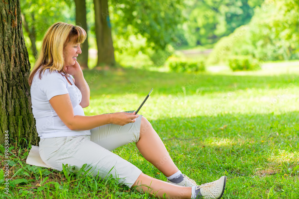 Happy mature woman in the park with a laptop Happy mature woman in the park with a laptop