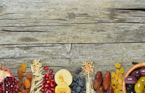 Dried fruits, barley, wheat, olives, pomegranate on a wooden table - symbols of judaic holiday Tu Bishvat .Copyspace background. Top view 