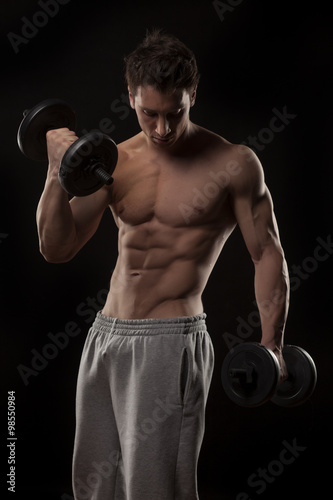 muscular young man with weights on a black background © vladimirfloyd