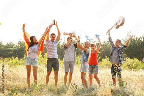 Joyful smiling friends dancing with raised hands in the forest outdoors