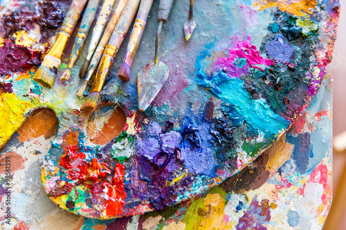 Closeup of art palette with colorful mixed paints and paintbrushed