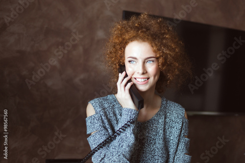 Beautiful happy woman talking on landline telephone in the room photo