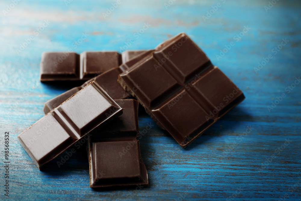 Black chocolate pieces on color wooden background Black chocolate pieces on color wooden background