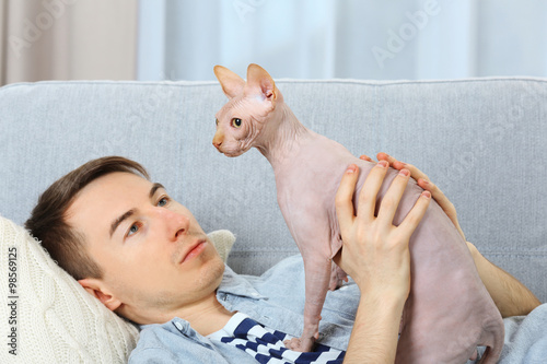 Young handsome man lies with cat on couch at home