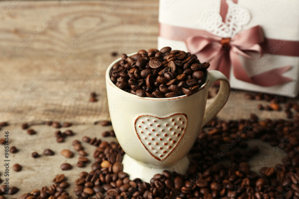 Beautiful gift with bow and coffee grains in mug, on wooden background Beautiful gift with bow and coffee grains in mug, on wooden background