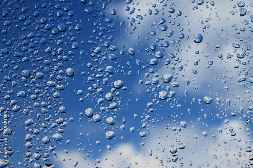 Rain drops on window with blue cloudy sky in background Rain drops on window with blue cloudy sky in background