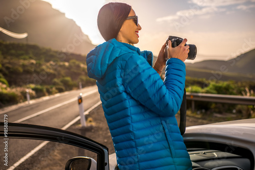 Female traveler photographing sunrise near the car