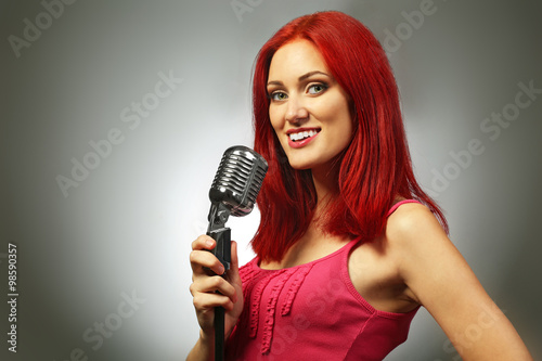 Beautiful young woman with microphone on gray background