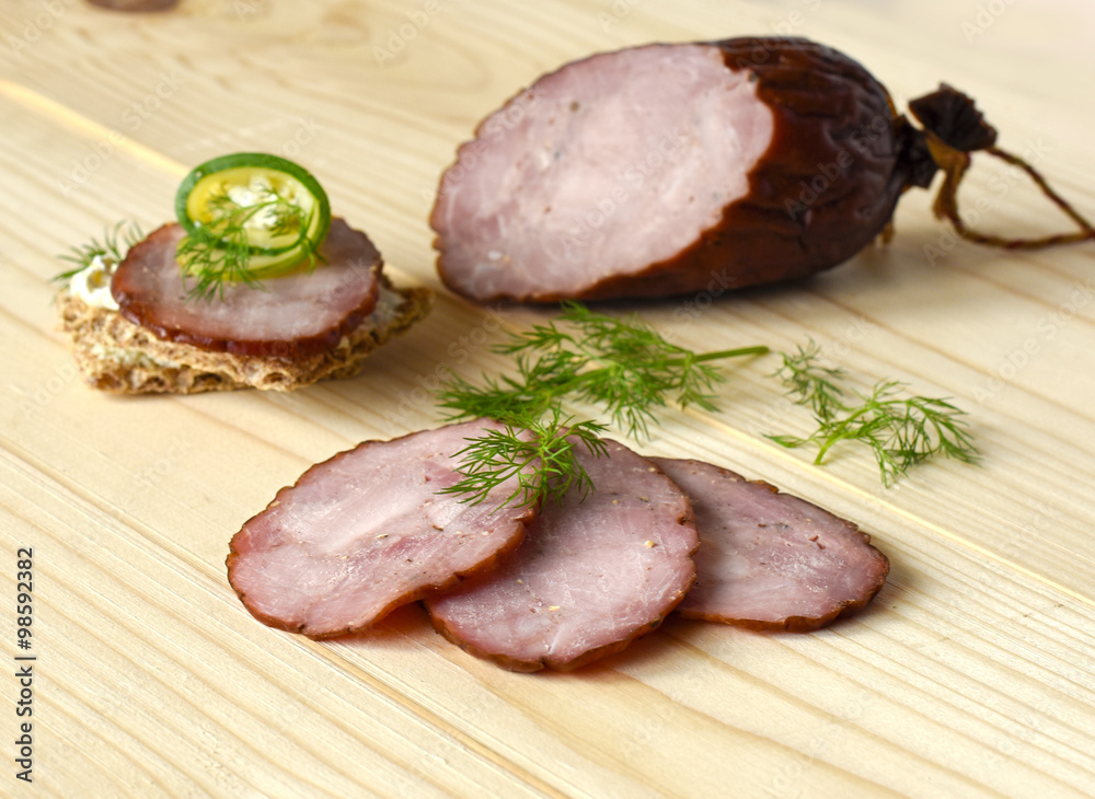 Traditional smoked sausage with dill, sandwich and vegetables on a wooden cutting board Traditional smoked sausage with dill, sandwich and vegetables on a wooden cutting board
