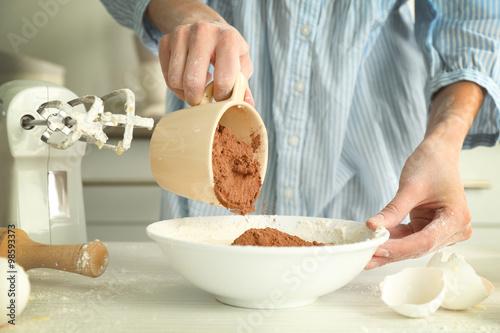 Woman is adding cocoa to the dough