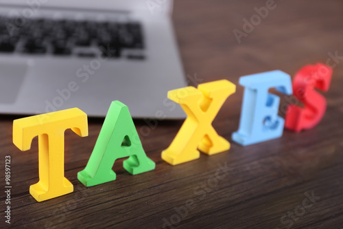 Alphabet TAXES and laptop on wooden table