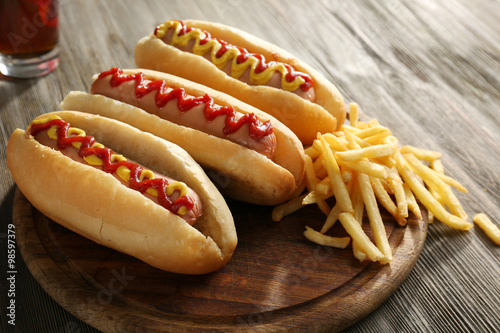 Foto Delicious hot-dogs with French fries on wooden chopping board, close up