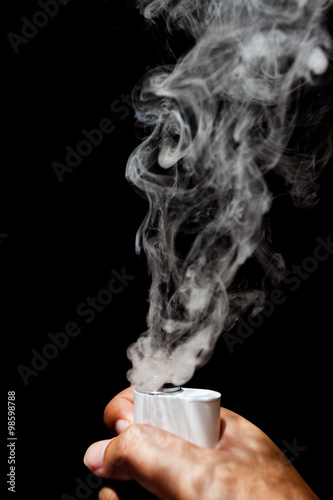 Electronic Cigarette or vaper is activating and release a cloud in a human hand, black color background