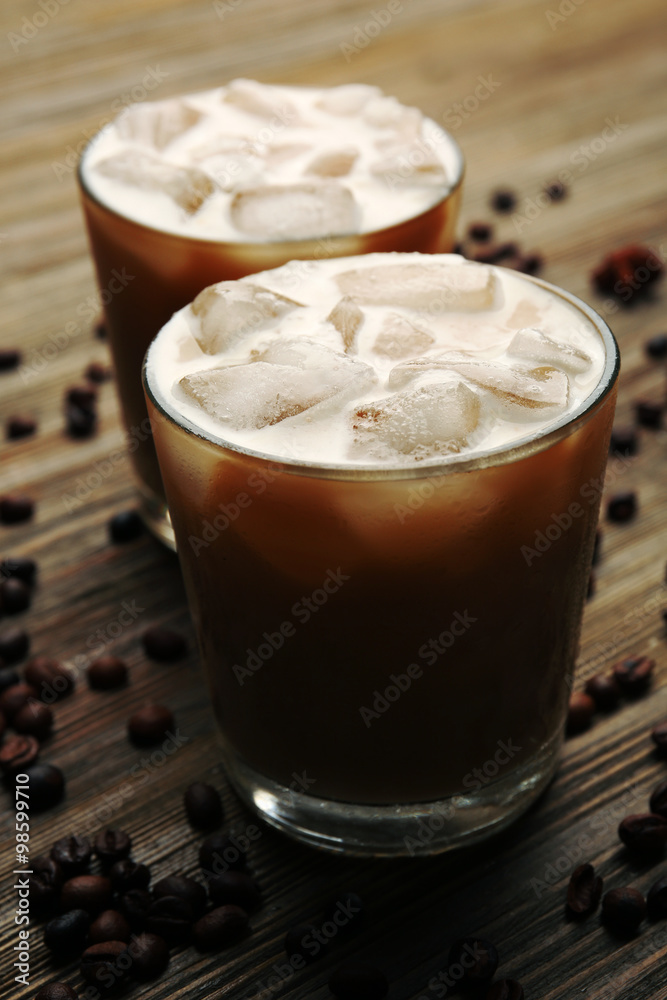 Two cups of ice coffee with coffee beans on wooden table