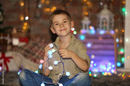 Little boy in light garland at home on a Christmas background