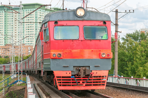 Red and grey suburban electric train moves towards on railroad turn vanishing against skyline background. Moscow, Russia. 
