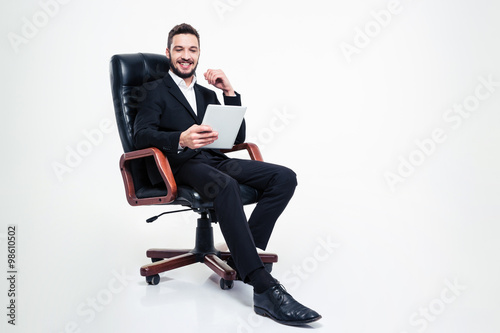 Cheerful businessman sitting in office chair and using tablet