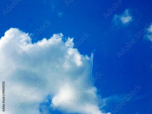 Airplane with chemtrails on partly cloudy sky