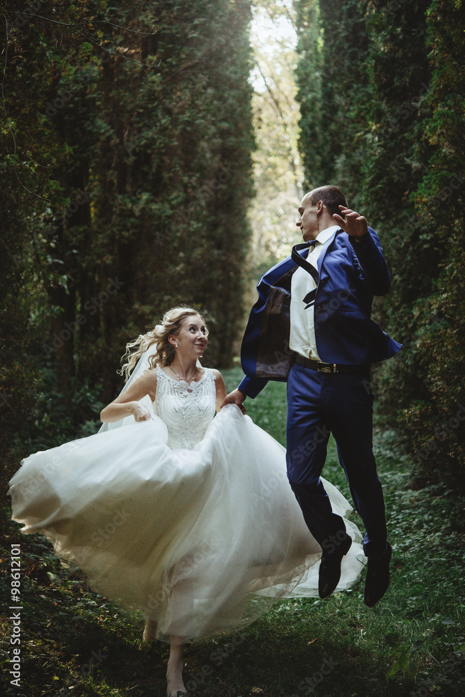 happy bride running and elegant groom on a background of beautiful sunny trees in  a forest