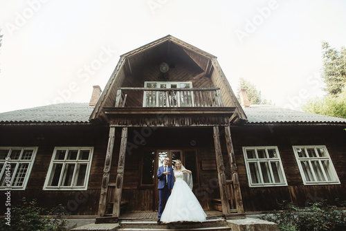 gorgeous stylish happy blonde bride and elegant groom near wooden cabin