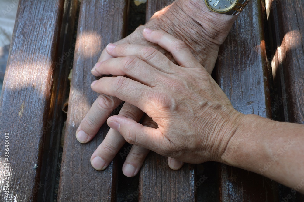 Obraz premium Old and Adult Hands. Hands of a fateher and his daughter on a wooden bench in the street.