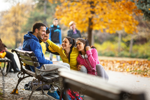  The group of friends, invigorated from their jog, find a park bench to relax, sharing laughter and stories as they enjoy the pleasant autumn day. © BalanceFormCreative