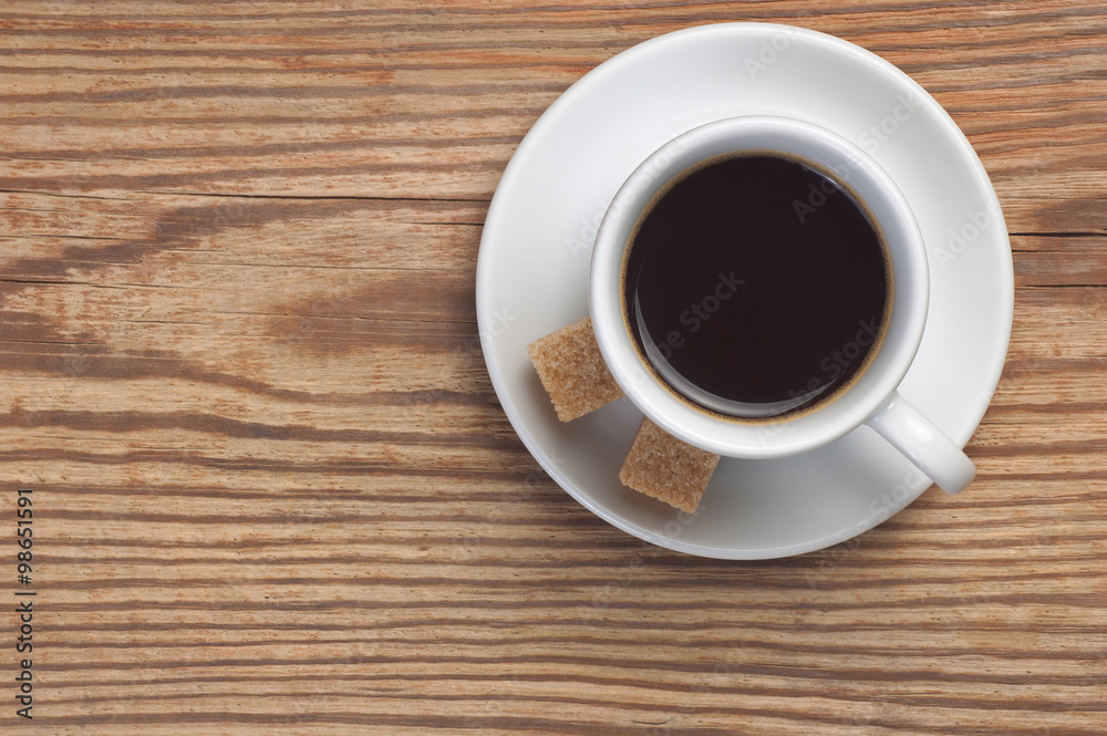 White saucer and cup of coffee with two cane sugar pieces on rustic wooden table background top view have place for text White saucer and cup of coffee with two cane sugar pieces on rustic wooden table background top view have place for text