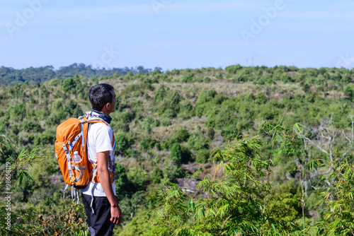Man hiker with orange backpack looking view of mountain.