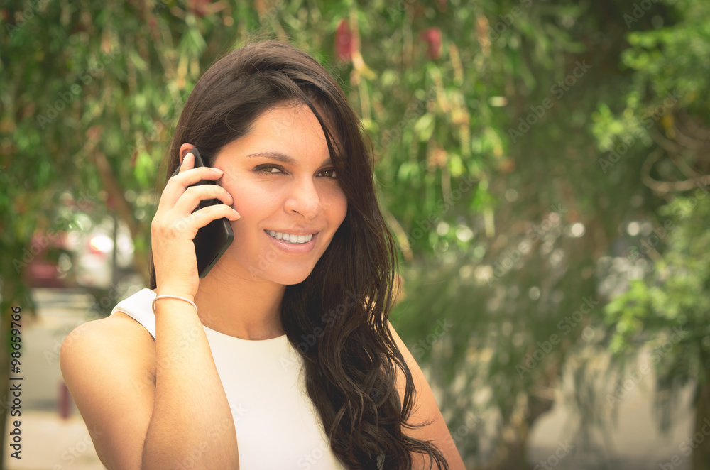 Classy attractive brunette wearing white dress talking on the phone in outdoors environment Classy attractive brunette wearing white dress talking on the phone in outdoors environment