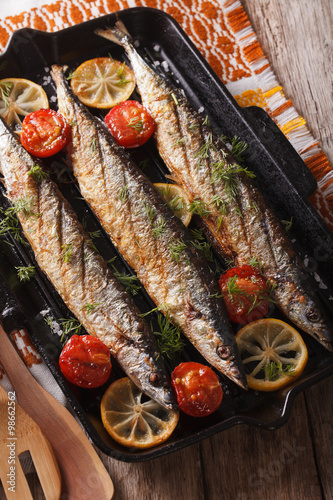 saury grilled with lemon and tomato on a grill pan close-up. Vertical
