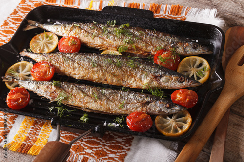 saury grilled with lemon and tomato on a grill pan close-up. horizontal
