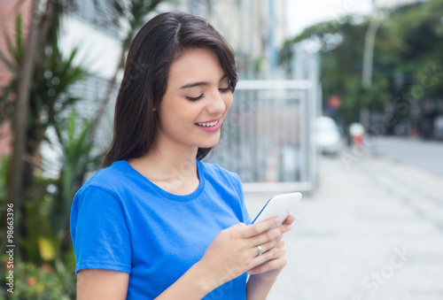 Attraktive Frau mit blauem Shirt in der Stadt surft mit Handy