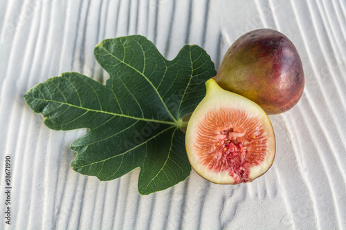 half cut black genoa figs and leaf on grey wooden background