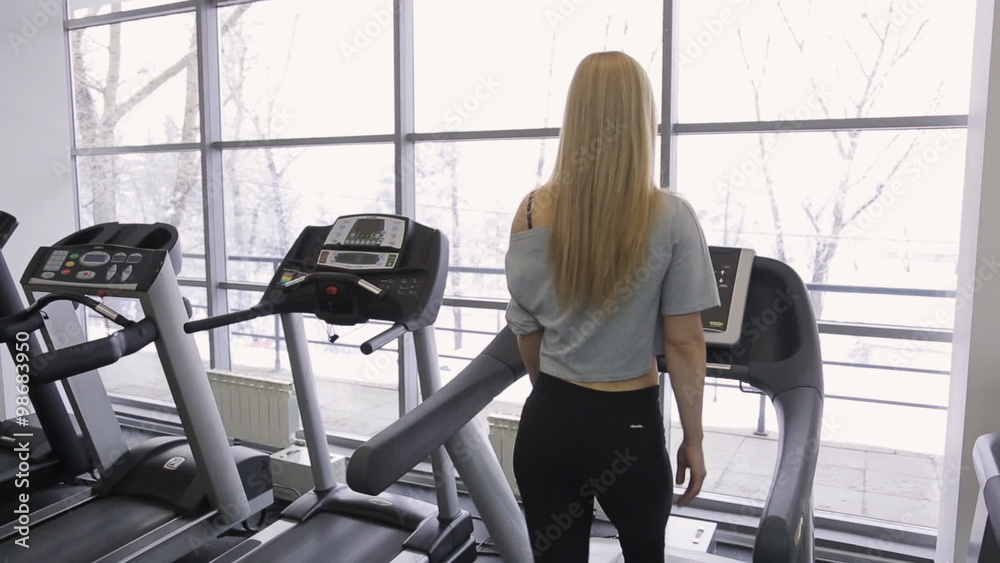 athlete sexy woman walking on a treadmill in the gym in front of