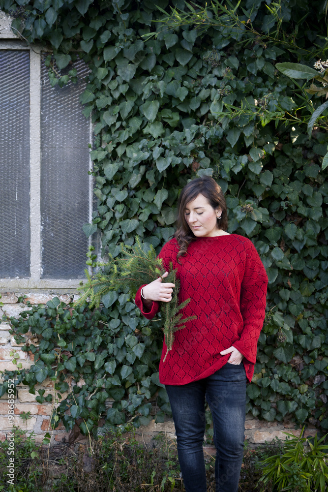 Fototapeta premium A woman holding in her arms pine branches in front of a wall covered with ivy leaves