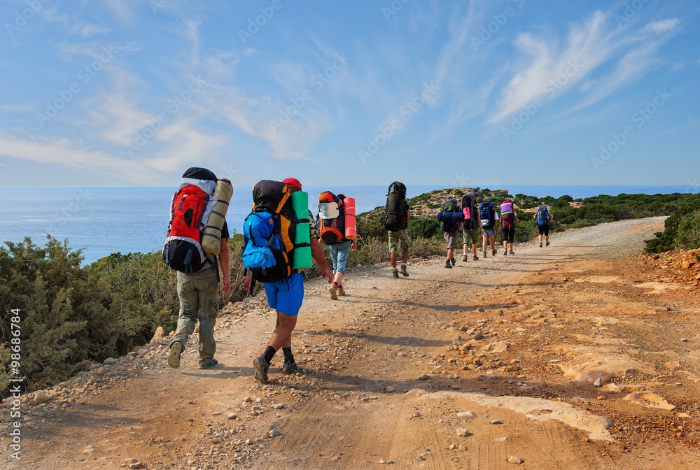group of tourists with large backpacks are on road sea - obrazy, fototapety, plakaty 