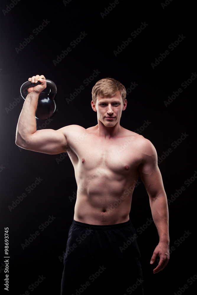 Handsome muscular guy with kettlebells isolated on black background